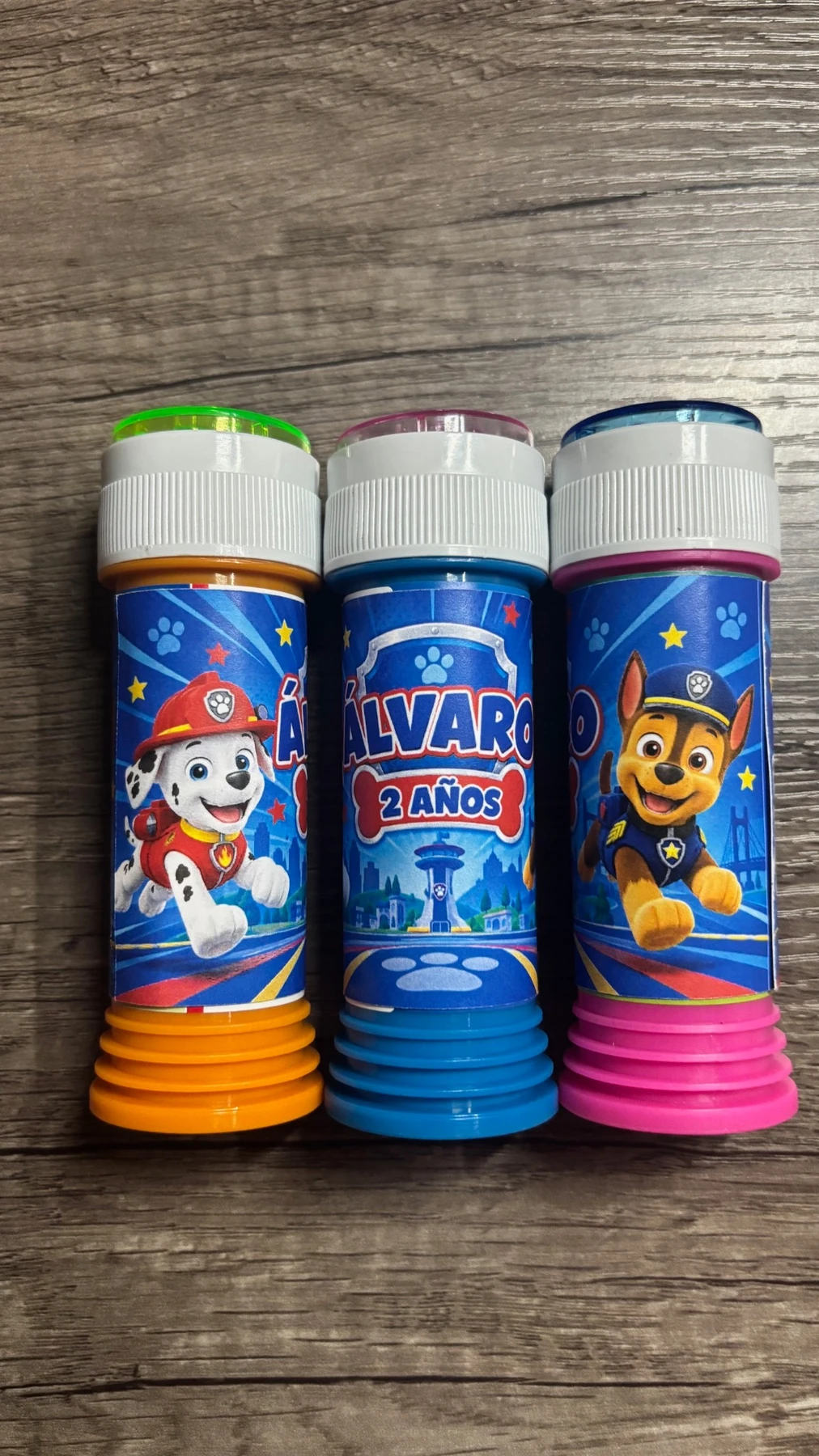 Tres pomperos de colores con etiquetas personalizadas de Patrulla Canina para el cumpleaños de Álvaro